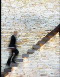 Book cover for "Step of Strength" by Courtney Valenzuela, featuring a person in a dark suit climbing a modern, floating wooden staircase mounted against a textured stone wall, captured with a motion blur effect to suggest upward movement.